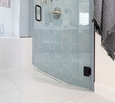 Closeup of curbless shower entry with tiled bench and hexagonal light-blue tiled walls.