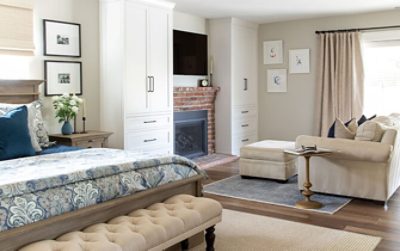 Traditionally styled room with wood floors, a neutral and blue color scheme, bed, fireplace and seating area.