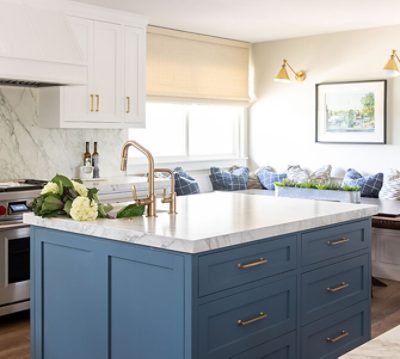 Kitchen with large center island and banquette dining area with white and blue decor, a marble-look backsplash, and gold hardware.
