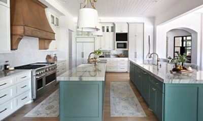 Spacious kitchen with two parallel marble-topped islands painted blue-green, white ceiling-height cabinets and a statement range hood.