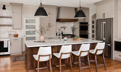 Modern kitchen with ceiling-height cabinets painted in a mid-tone gray-beige color with dark wood and matte black accents and white dining chairs at the large kitchen island.