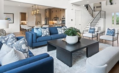 Modern living room with blue sofas, square coffee table, open kitchen, and staircase in the background featuring walls painted Pure White by Sherwin-Williams.