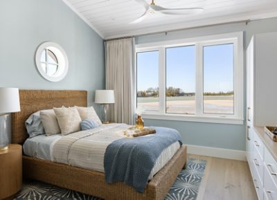 Coastal-themed bedroom with a wicker bed, large window, and beach view featuring walls painted Niebla Azul and Pure White trim.