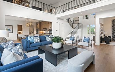 Modern living room with blue sofas, square coffee table, open kitchen, and staircase in the background featuring walls painted Pure White by Sherwin-Williams.