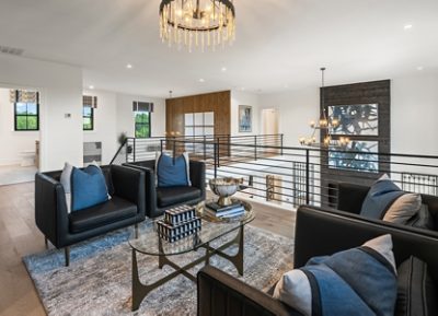 Lounge area in the upstairs landing of a modern home featuring black armchairs, a glass coffee table, and a decorative chandelier with walls painted Pure White by Sherwin-Williams.