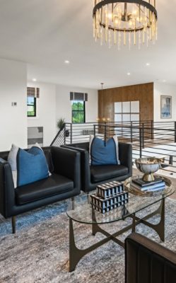 Lounge area in the upstairs landing of a modern home featuring black armchairs, a glass coffee table, and a decorative chandelier with walls painted Pure White by Sherwin-Williams.