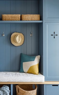 Detail shot of a cushioned bench, decorative pillows, hooks, and baskets in a built-in painted blue using Sherwin-Williams Stargazer.