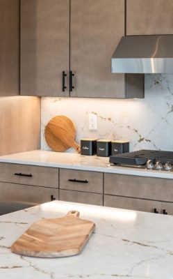 Modern kitchen with a marble-look quartz countertop, black-labeled canisters, a wooden cutting board, and a stainless steel stove.