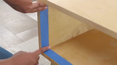 A person using masking tape on a coffee table.