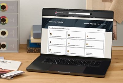 An open laptop and Sherwin-Williams color tools on a wooden desktop with the Design+ dashboard featured on screen.