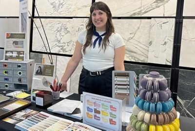 Woman in a white shirt and dark pants smiling while standing at a table with an array of Sherwin-Williams color tools and tiered display of colorful macarons.