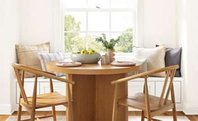 Naturally lit dining nook area with wood table and chairs in front of a window bench seat.