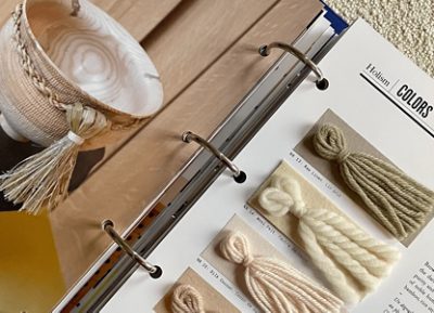 Closeup of a ring-bound trend book from NellyRodi on the topic of Holism, with sample tassels of yarn in a range of neutral colors juxtaposed with a decorative wooden bowl.