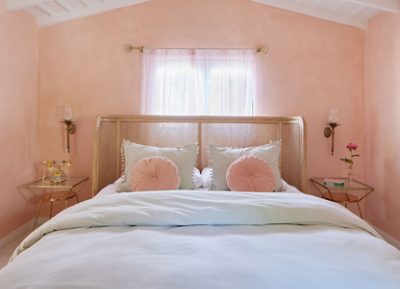 Bedroom painted Sherwin-Williams Jovial in a limewash technique with slightly vaulted ceiling, transparent curtains, and glass bedside tables and antique sconces flanking the bed.