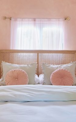 Bedroom painted Sherwin-Williams Jovial in a limewash technique with slightly vaulted ceiling, transparent curtains, and glass bedside tables and antique sconces flanking the bed.