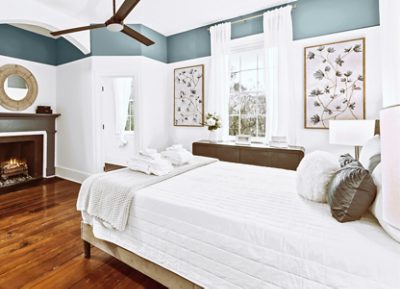 Bedroom with a white bedspread, fireplace, large window, and decorative accents in blue and white, featuring Sherwin-Williams Morning at Sea and Stargazer.