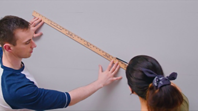 A man and woman measuring and marking a wall.