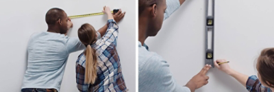 A man and a woman measuring and marking their white bathroom wall in preparation for wallpaper application.