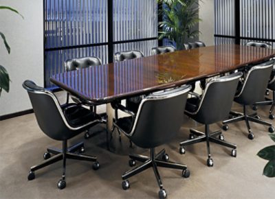 An office meeting room with a long wooden table, chairs, plants and floor to ceiling windows.