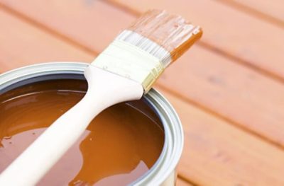 Open can of Minwax wood stain on a deck with a paint brush on top.