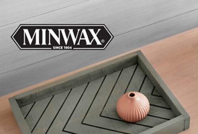 Minwax. Three colored wood stains on different wooden surfaces stacked on top of each other with a small brown vase on top. 