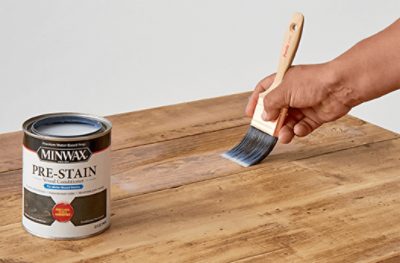 A person applying Minwax Pre-Stain to a table top with a brush.