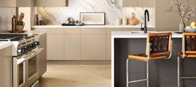 A modern kitchen with earth toned cabinets, marble backsplash, and chairs in front of an island