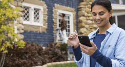 A woman smiling at her phone with a painter in the background.