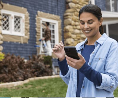A woman smiling at her phone with a painter in the background.