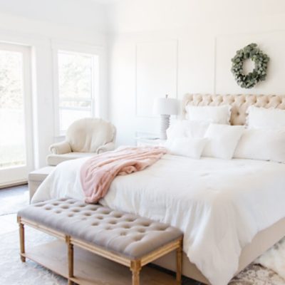 A bright, light neutral bedroom with an upholstered headboard and bench at the bottom of the bed.