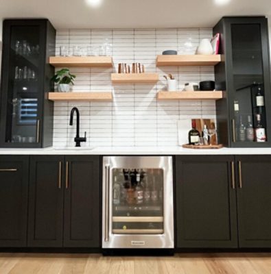 A small kitchen area with narrow white subway tile between black glass-front cabinets sitting on a bottom cabinet section painted the same black hue.