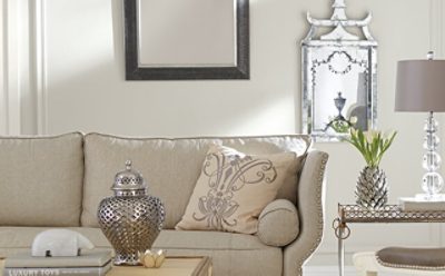 A beige living room wall with three mirrors and the top of a couch cushion