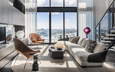 Modern urban loft living area with postmodern sectional and twin leather armchairs in front of flat screen TV with a view to an outside balcony area overlooking a city skyline.