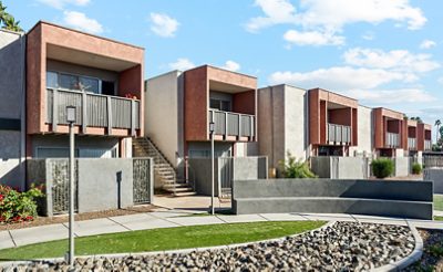 Row of modern apartment buildings with balconies, stucco finish, and landscaped foreground, featuring the Sherwin-Williams colors Reddened Earth, Anew Gray, and Tricorn Black.