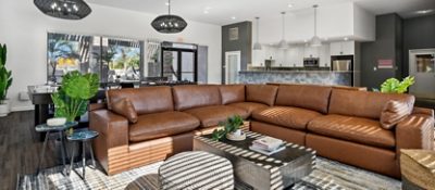 Interior of apartment complex clubhouse recreation room with a large brown leather sectional, wooden coffee table, and open kitchen area in background, featuring Sherwin-Williams colors Westchester Gray, Pure White, and High Reflective White.