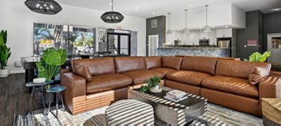 Interior of apartment complex clubhouse recreation room with a large brown leather sectional, wooden coffee table, and open kitchen area in background, featuring Sherwin-Williams colors Westchester Gray, Pure White, and High Reflective White.