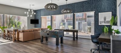 Interior of apartment complex clubhouse recreation room with large windows, a large brown leather sectional and game tables in the foreground, featuring Sherwin-Williams paint color Westchester Gray.