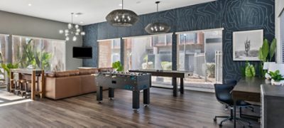 Interior of apartment complex clubhouse recreation room with large windows, a large brown leather sectional and game tables in the foreground, featuring Sherwin-Williams paint color Westchester Gray.