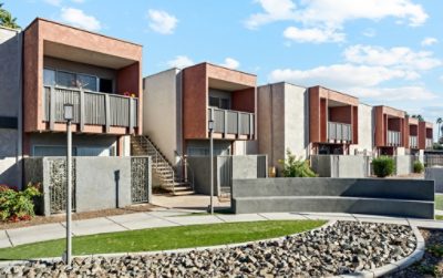 Row of modern apartment buildings with balconies, stucco finish, and landscaped foreground, featuring the Sherwin-Williams colors Reddened Earth, Anew Gray, and Tricorn Black.