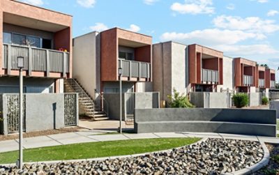 Row of modern apartment buildings with balconies, stucco finish, and landscaped foreground, featuring the Sherwin-Williams colors Reddened Earth, Anew Gray, and Tricorn Black.