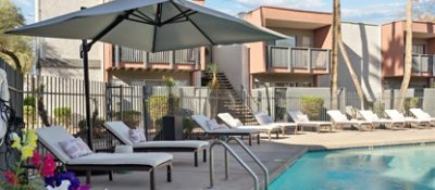 Outdoor pool area with lounge chairs and large umbrella, adjacent to a residential apartment building.