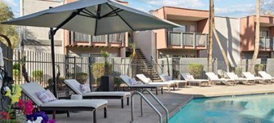 Outdoor pool area with lounge chairs and large umbrella, adjacent to a residential apartment building.