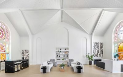 The interior of a former church sanctuary repurposed as a spacious interior design studio with stained glass windows, minimalist black and white furniture, and high vaulted ceilings and walls painted Alabaster by Sherwin-Williams.