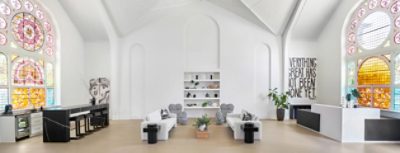 The interior of a former church sanctuary repurposed as a spacious interior design studio with stained glass windows, minimalist black and white furniture, and high vaulted ceilings and walls painted Alabaster by Sherwin-Williams.