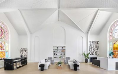 The interior of a former church sanctuary repurposed as a spacious interior design studio with stained glass windows, minimalist black and white furniture, and high vaulted ceilings and walls painted Alabaster by Sherwin-Williams.