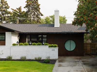 Exterior of Aly and Jason’s house with white brick and dark wood facade, circular window, and white chimney. 