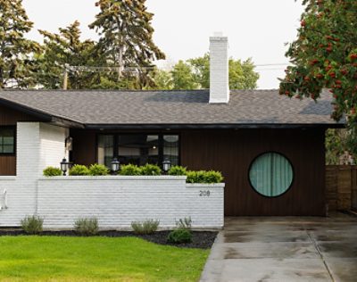 Exterior of Aly and Jason’s house with white brick and dark wood facade, circular window, and white chimney. 