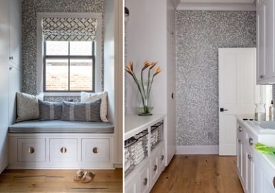 A cozy window seat with gray pillows and geometric wallpaper, next to a narrow laundry room with bird of paradise flowers in a vase and white cabinetry. 
