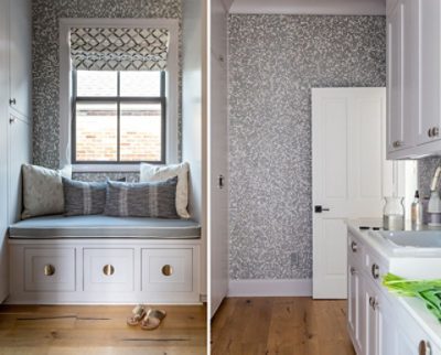 A cozy window seat with gray pillows and geometric wallpaper, next to a narrow laundry room with bird of paradise flowers in a vase and white cabinetry. 