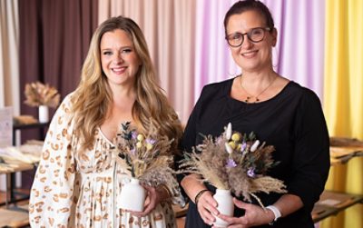 Shown on left, flat lay of the dried florals on a white background next to color sample chips of the Color Capsule of the Year colors. Shown on right, two women smile holding their dried-flower bouquets in small white vessels in front of a curtained backdrop in various Color Capsule of the Year hues.